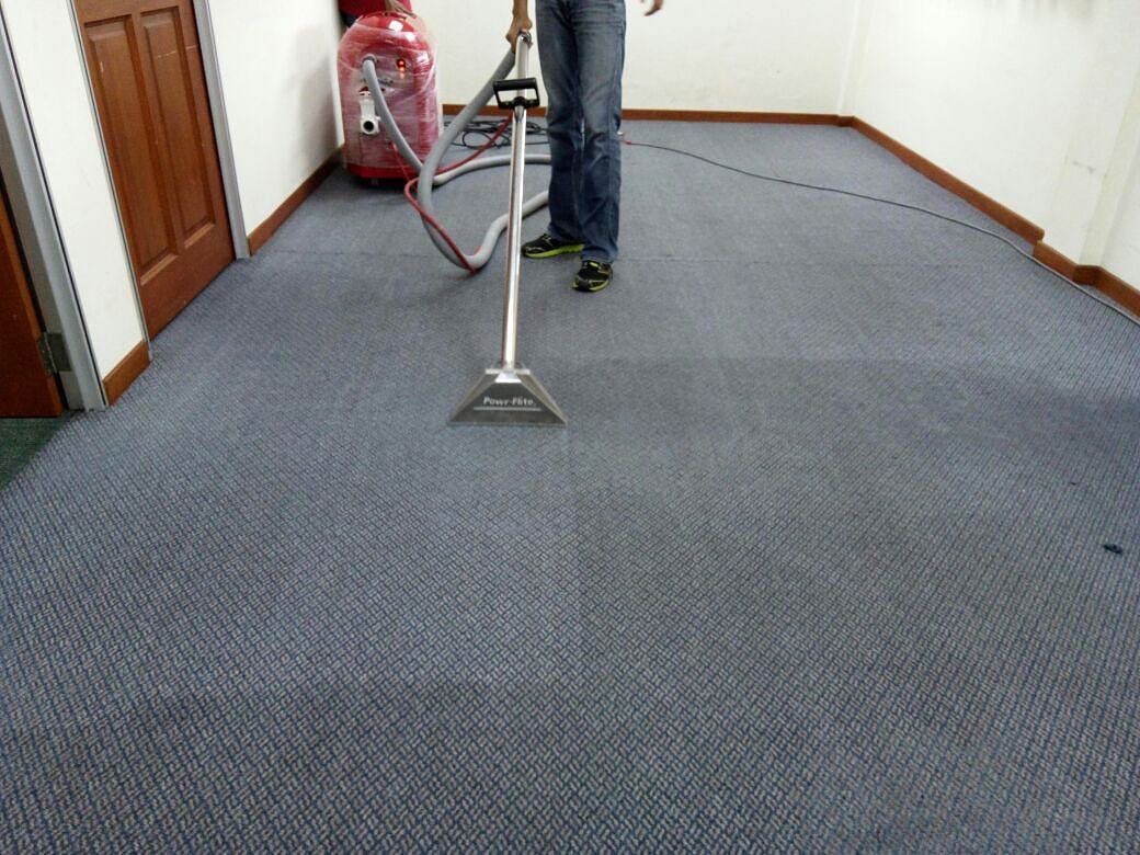 Portable carpet extraction machine with a hose and floor-cleaning wand in use on fitted carpet